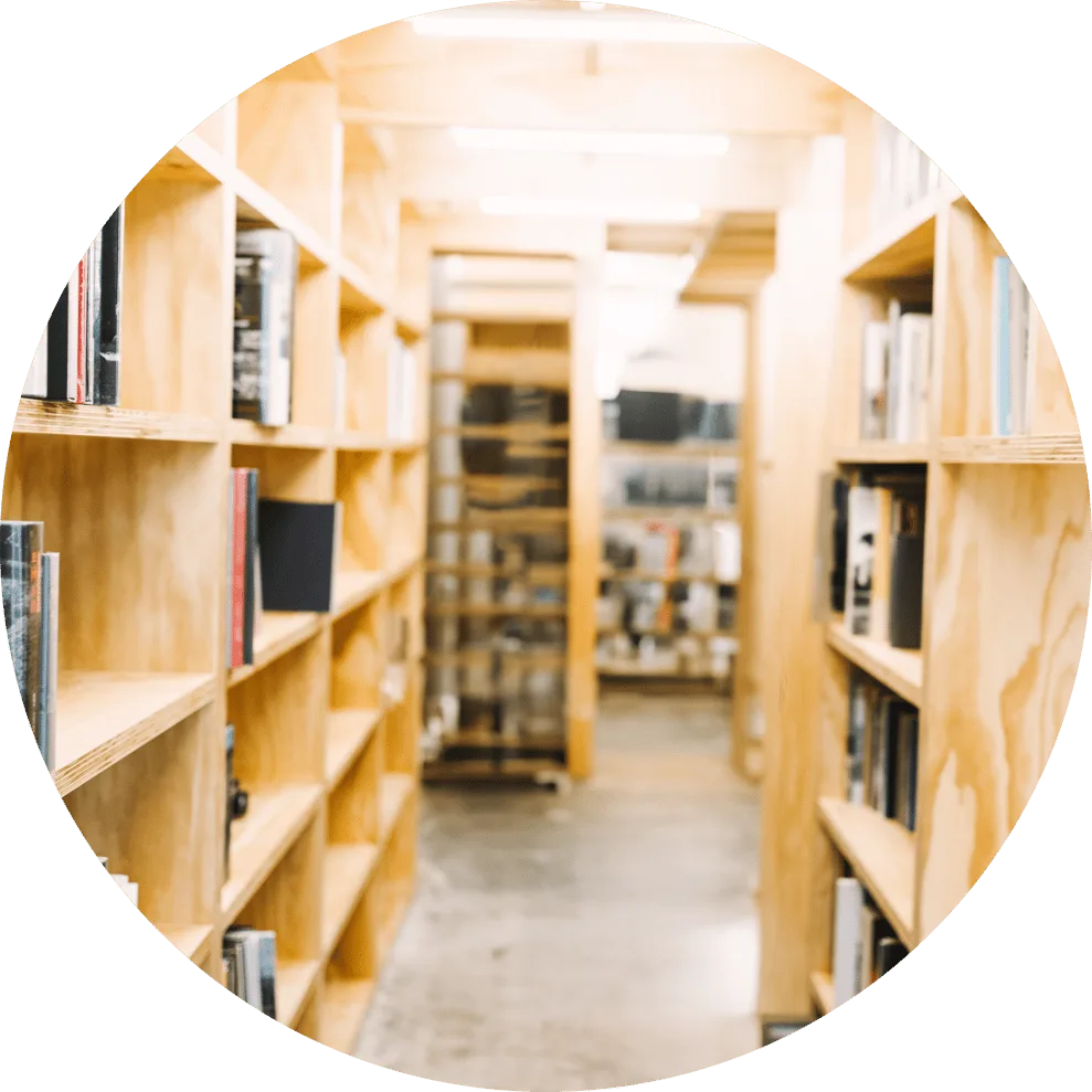 写真：木製の本棚が並ぶ図書館の通路。明るい木目の棚に多数の本が並んでいる様子