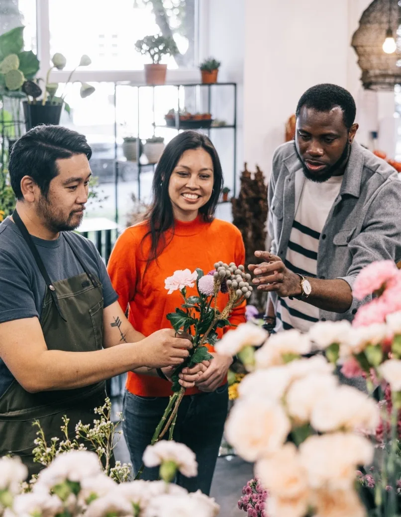 写真：花屋で花束を作る3人の多様な従業員。アジア系の男性、ラテン系の女性、アフリカ系の男性が協力している