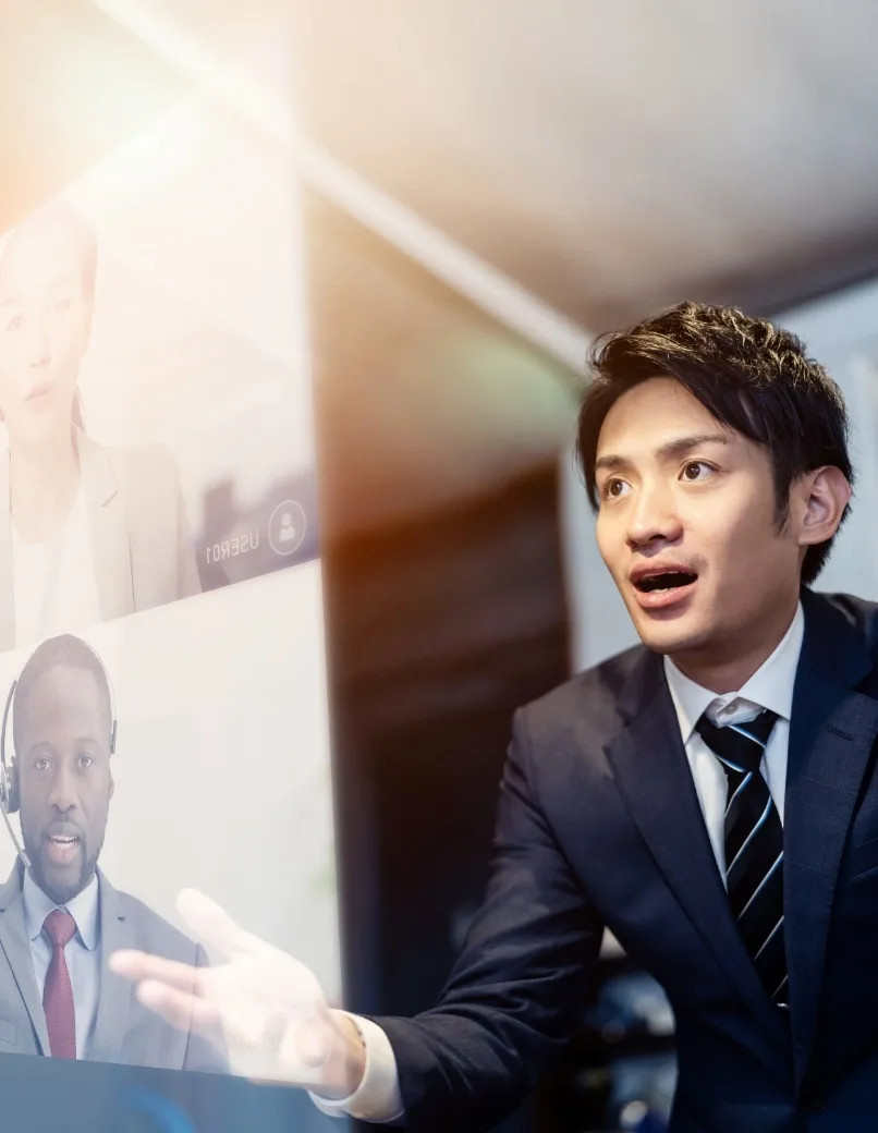 写真：オンラインビデオ会議中のアジア人ビジネスマン。画面には黒人男性の同僚が映っている