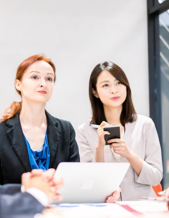 写真:2人の女性が会議室でノートパソコンを使いながら会話している。
