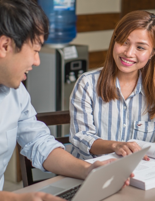 写真:学習資料を見ながら会話をする男女。明るい笑顔と親しみやすい雰囲気が印象的な教室内の一場面。