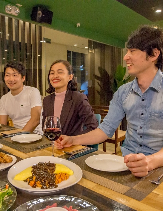 写真:夕食の場でリラックスした雰囲気の生徒たちが、笑顔で食事を楽しんでいる。テーブルには多彩な料理が並べられている。